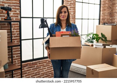 Middle Age Woman Moving To A New Home Holding Cardboard Box Relaxed With Serious Expression On Face. Simple And Natural Looking At The Camera. 