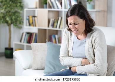 Middle Age Woman In Pain Suffering A Stomach Ache Holding Tummy Sitting On The Sofa At Home