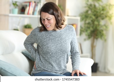 Middle Age Woman In Pain Suffering Backache Stting On A Couch At Home