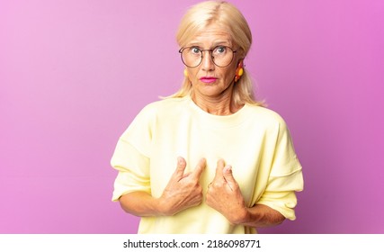 Middle Age Woman Pointing To Self With A Confused And Quizzical Look, Shocked And Surprised To Be Chosen