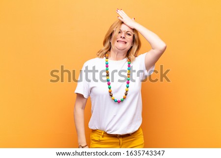 middle age woman raising palm to forehead thinking oops, after making a stupid mistake or remembering, feeling dumb