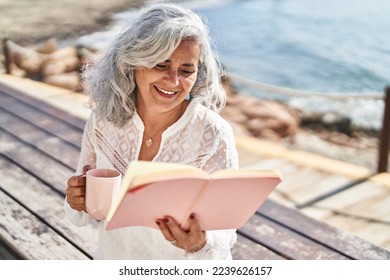 Middle age woman reading book and drinking coffee sitting on bench at seaside - Powered by Shutterstock