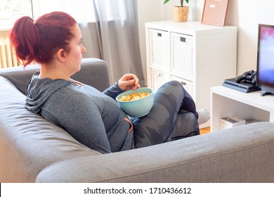 Middle age woman relaxing on the sofa, watching TV and  eating chips