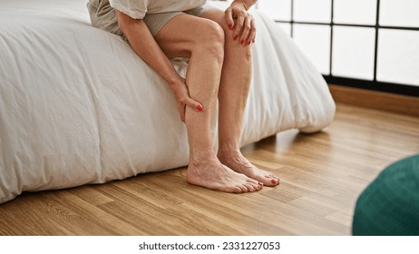 Middle age woman sitting on bed tired massaging legs at bedroom - Powered by Shutterstock