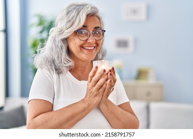 Middle age woman smelling aromatic candle at home