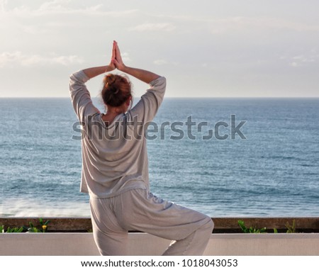 Middle age woman standing on the terrace practicing Qigong and yoga exercises, view of the Pacific ocean, Durban