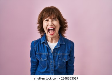 Middle age woman standing over pink background angry and mad screaming frustrated and furious, shouting with anger. rage and aggressive concept.  - Shutterstock ID 2248853019