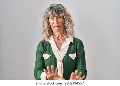 Middle age woman standing over white background disgusted expression, displeased and fearful doing disgust face because aversion reaction. 