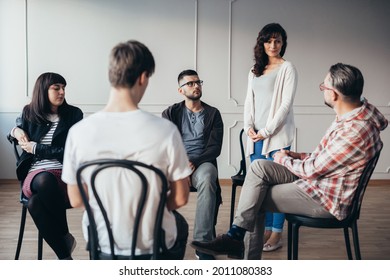 Middle Age Woman Stands In Front Of A Group Of People During A Therapy Meeting And Talks About Her Family Problems