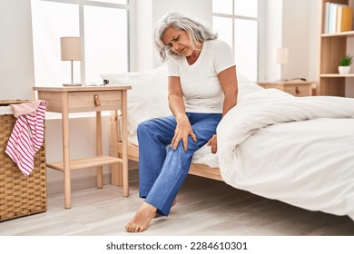 Middle age woman suffering for knee pain sitting on bed at bedroom - Powered by Shutterstock