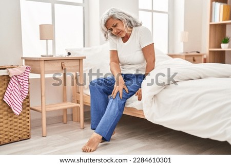 Middle age woman suffering for knee pain sitting on bed at bedroom