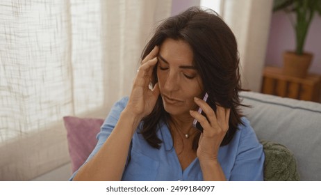 Middle age woman talking on phone with hand on head, sitting in living room at home, showing stress or worry in an indoor apartment setting. - Powered by Shutterstock