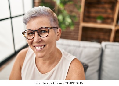 Middle age woman using hearing aid sitting on sofa at home - Powered by Shutterstock