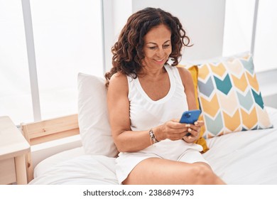 Middle age woman using smartphone sitting on bed at bedroom - Powered by Shutterstock