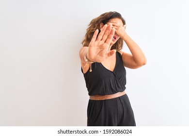 Middle age woman wearing black casual dress standing over isolated white background covering eyes with hands and doing stop gesture with sad and fear expression. Embarrassed and negative concept.