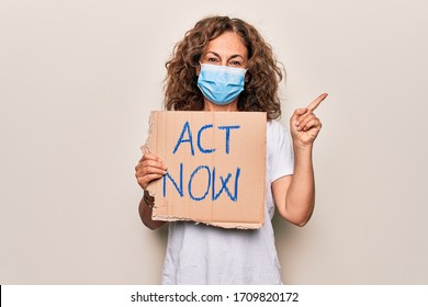 Middle Age Woman Wearing Coronavirus Protection Mask Holding Act Now Protest Cardboard Smiling Happy Pointing With Hand And Finger To The Side