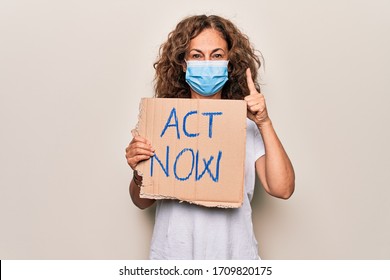 Middle Age Woman Wearing Coronavirus Protection Mask Holding Act Now Protest Cardboard Smiling With An Idea Or Question Pointing Finger With Happy Face, Number One