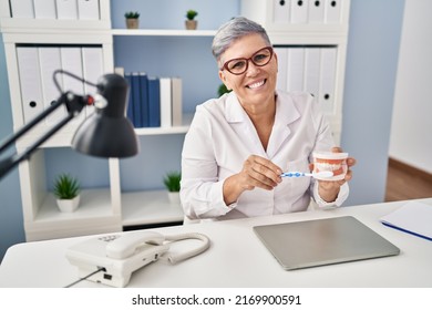 Middle Age Woman Wearing Dentist Uniform Teaching To Wash Tooth At Clinic