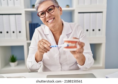 Middle Age Woman Wearing Dentist Uniform Teaching To Wash Tooth At Clinic