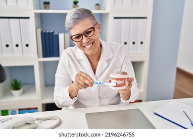 Middle Age Woman Wearing Dentist Uniform Teaching To Wash Tooth At Clinic