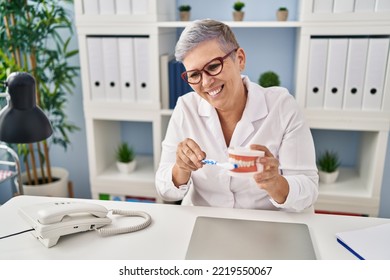 Middle Age Woman Wearing Dentist Uniform Teaching To Wash Tooth At Clinic