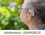 Middle age woman wearing eyeglasses and using hearing aid while sitting on chair in the garden at home. The problem of hearing in old age concept.