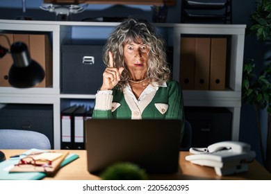 Middle Age Woman Working At Night Using Computer Laptop Pointing Finger Up With Successful Idea. Exited And Happy. Number One. 