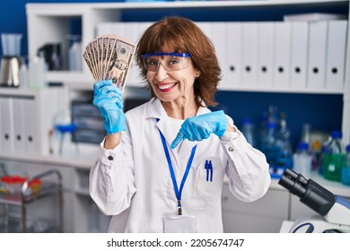 Middle Age Woman Working At Scientist Laboratory Holding Money Pointing Finger To One Self Smiling Happy And Proud 