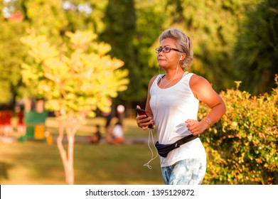 Middle Aged 40s Or 50s Happy And Attractive Woman With Grey Hair Training At City Park With Green Trees On Sunrise Doing Running And Jogging Workout In Health Care Fitness And Healthy Lifestyle