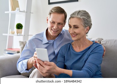 Middle aged 50s senior couple holding device looking at smartphone using mobile apps tech, shopping in ecommerce application, ordering delivery, buying goods online on cell phone sit on sofa at home. - Powered by Shutterstock