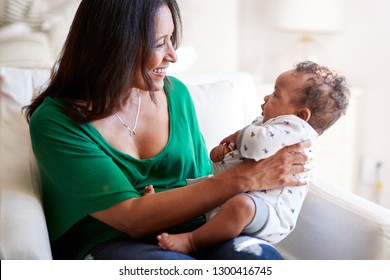 Middle aged African American grandmother sitting in an armchair holding her three month old grandson and smiling, focus on foreground