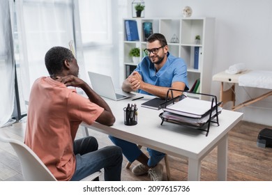 Middle Aged African American Man Touching Neck During Consultation With Positive Physiotherapist