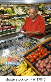 Middle Aged African American Man In Grocery Store Writing On Shopping List.