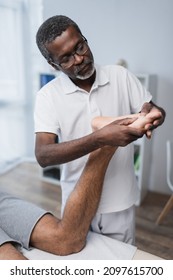 Middle Aged African American Physical Therapist Massaging Foot Of Man In Rehab Center