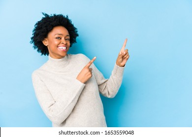 Middle aged african american woman against a blue background isolated pointing with forefingers to a copy space, expressing excitement and desire.
