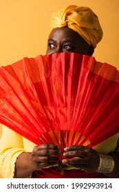 Middle Aged African American Woman Covering Face With Red Fan On Yellow