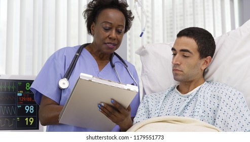 Middle aged African nurse taking notes of male patients current health condition