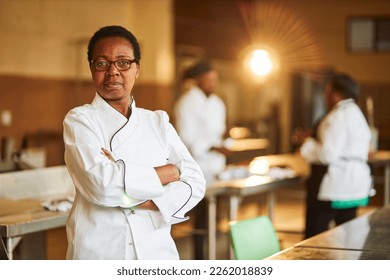 middle aged african with short hair chef wearing full chefs outfit with glasses in a commercial kitchen arms crossed - Powered by Shutterstock