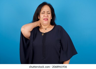 Middle Aged Arab Woman Standing Against Blue Background Suffering From Back And Neck Ache Injury, Touching Neck With Hand, Muscular Pain.