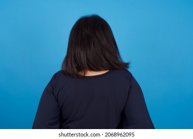 Middle Aged Arab Woman Standing Against Blue Background Standing Backwards Looking Away With Arms On Body.