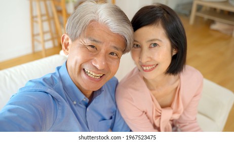 middle aged asian couple taking selfie in the living room - Powered by Shutterstock