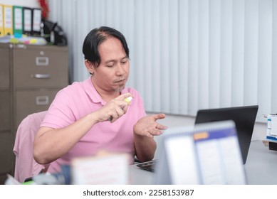 A middle aged asian employee sprays alcohol on his hands. Disinfecting protocol at the office. - Shutterstock ID 2258153987