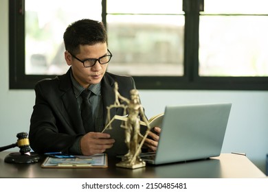 Middle aged Asian male lawyer working on laptop and legal contract documents in courtroom Judge's Hammer and Goddess Scales concept of legal counseling and services.