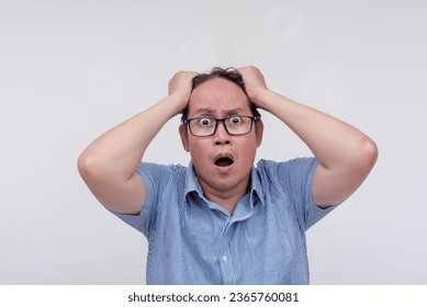 A middle aged asian man pulling his hair in worry. Extremely stressed out. Isolated on a white backdrop.