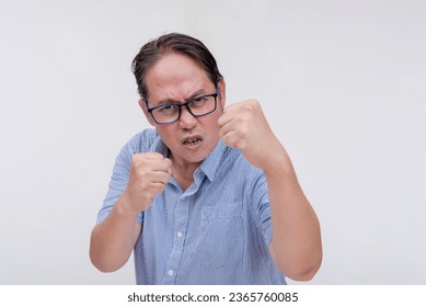 A middle aged asian man threatens to hit someone with his fist if they come closer. A hotheaded dad putting his guard stance up. Isolated on a white backdrop. - Shutterstock ID 2365760085
