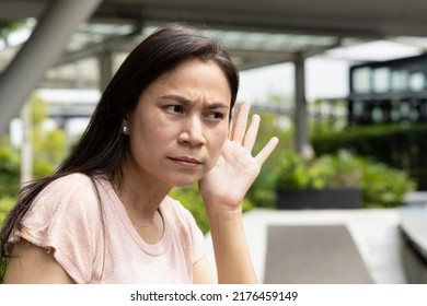 Middle aged asian senior woman listening to rumor, gossip, hearsay, concept image of fake news, propaganda or news manipulation - Shutterstock ID 2176459149