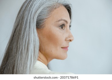 Middle Aged Asian Woman With Beautiful Straight Hoary Hair Poses On Light Grey Background In Studio Closeup Side View. Mature Beauty Lifestyle