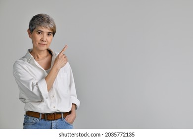 Middle aged Asian woman pointing fingers up at empty copy space for text isolated on white background. looking at the camera