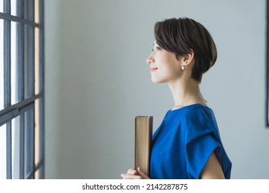 Middle Aged Asian Woman Reading A Book In Fashionable Room.