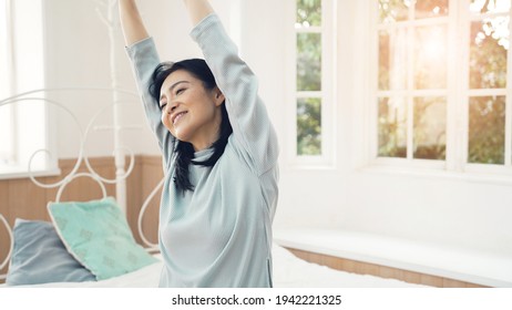 Middle Aged Asian Woman Waking Up In Bedroom. Stretch.